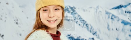 trendy little girl in warm stylish outfit smiling at camera with mountain backdrop, fashion, banner