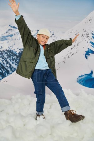 joyous little boy having fun and smiling cheerfully posing in motion on mountain backdrop, fashion