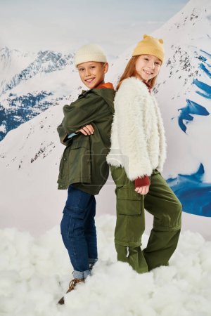 vertikale Aufnahme von netten Freunden in stylischer Winterbekleidung, die Rücken an Rücken posieren, in die Kamera lächeln, Mode