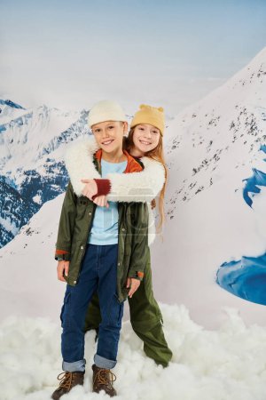 Vertikale Aufnahme von kleinen Freunden in winterlichen Outfits, die sich umarmen und in die Kamera lächeln, Modekonzept
