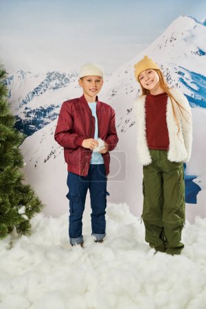 preadolescent adorable children in winter attire standing on snow smiling at camera, fashion concept
