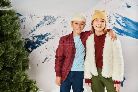 niño pequeño con la mano en el hombro de la chica sonriendo a la cámara, traje de invierno con estilo, concepto de moda