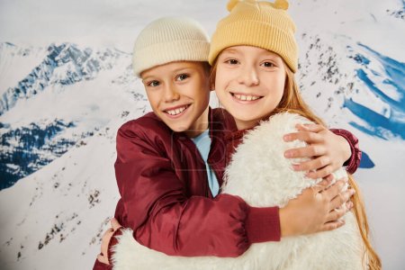 cheerful preadolescent children in stylish beanie hats hugging warmly and smiling at camera, fashion
