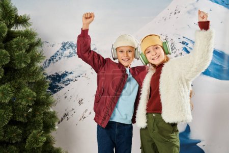 joyous little children in stylish jackets cheering with raised arms smiling at camera, fashion