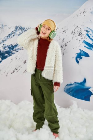 kleines Mädchen in stylischer Winterkleidung mit Kopfhörern, Musik hörend und fröhlich lächelnd, Mode