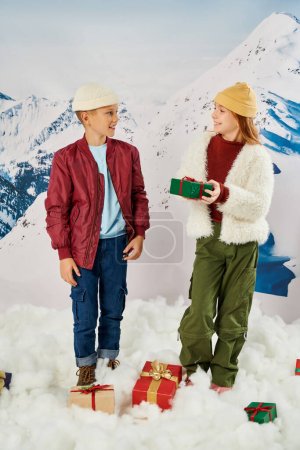 Kleines Mädchen hält Geschenk in der Hand und lächelt ihren Freund mit Berg auf dem Hintergrund an, Modekonzept