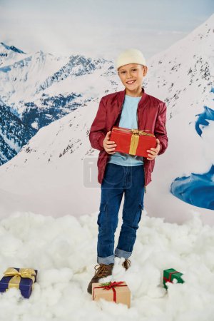 vertikale Aufnahme eines fröhlichen kleinen Jungen in roter Jacke, der Geschenke hält und in die Kamera lächelt, Mode