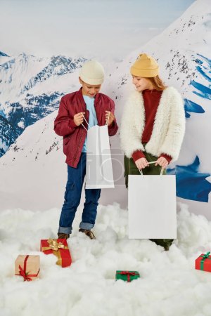 vertikale Aufnahme von kleinen Freunden in stylischer Winterkleidung, die in die Tasche schauen, Mode