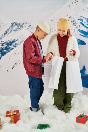 Vertikale Aufnahme von fröhlichen kleinen Freunden in stylischen Winterreifen, die glücklich in der Geschenktüte aussehen