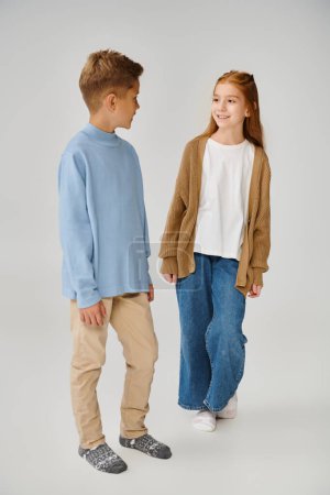 joyeuse petite fille en tricot cardigan souriant au garçon préadolescent en sweat-shirt bleu, concept de mode