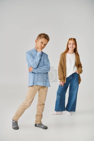 vertikale Aufnahme eines lustigen kleinen Mädchens in Strickjacke in der Nähe eines ernsten Jungen in blauem Sweatshirt