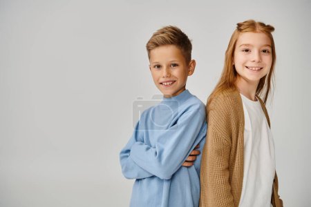 cheerful preteen children in casual warm attires posing back to back looking at camera, fashion