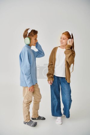 lustige vorpubertäre Freunde posieren mit Kopfhörern vor grauem Hintergrund und lächeln einander an, Mode