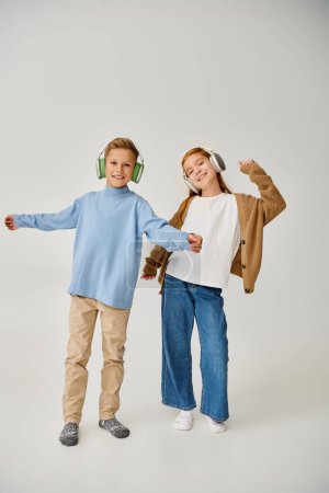 enfants préadolescents mignons dans des vêtements décontractés chauds avec des écouteurs posant en mouvement, souriant joyeusement