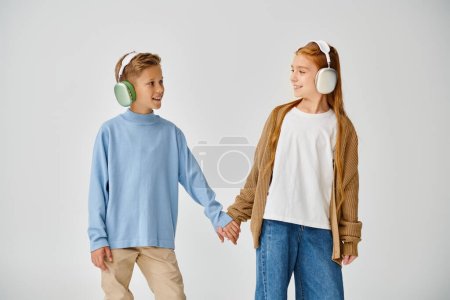preteen friends in casual attires with headsets holding hands and smiling at each other, fashion