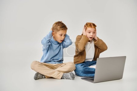 two scared trendy little children looking at laptop and closing ears with hands, fashion concept