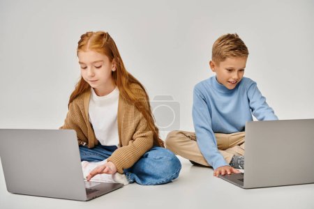 lindos niños preadolescentes en trajes de moda en el suelo mirando sus computadoras portátiles, concepto de moda