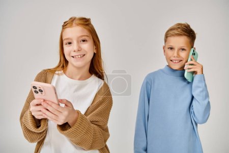 joyous little boy talking by phone next to his jolly peer smiling at camera, fashion concept