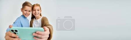 jolly little friends in warm trendy clothes taking selfie on gray backdrop, fashion concept, banner
