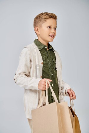 vertical shot in profile of preteen cute boy in casual attire holding present bags, fashion concept