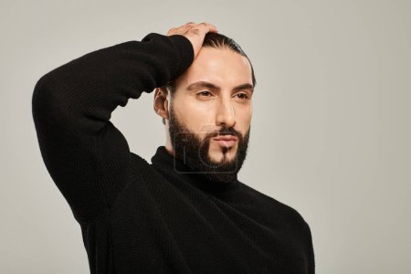 portrait of handsome arabic man with beard posing in black turtleneck on grey background