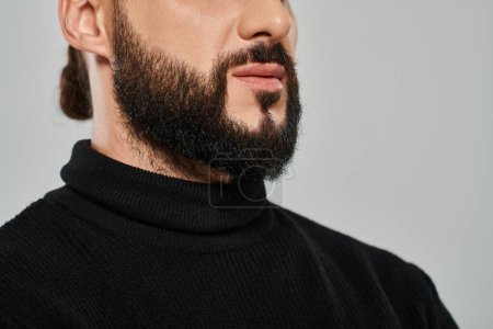 cropped view of masculine and bearded arabic man in black turtleneck on grey backdrop