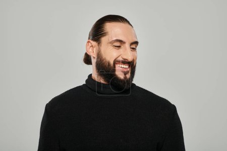Porträt eines gut aussehenden arabischen Mannes mit Bart, der im Rollkragen posiert und vor grauem Hintergrund lächelt