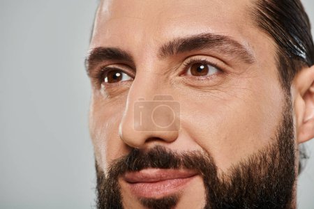 close up shot of happy bearded arabic man smiling and looking away on grey background
