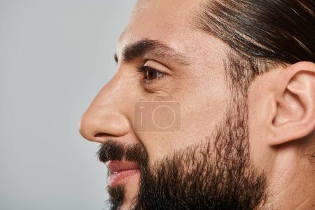 Photo for Profile of cheerful arabic man with beard smiling and looking away on grey background - Royalty Free Image