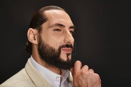 handsome bearded arabic man in white shirt and blazer looking away on black background