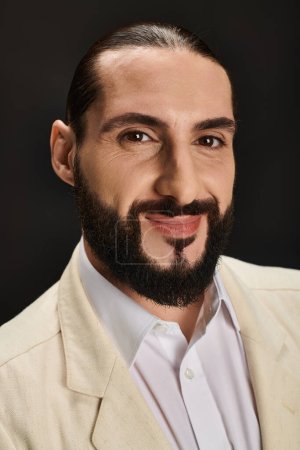 fröhlicher und bärtiger arabischer Mann in weißem Hemd und Blazer, der in die Kamera auf schwarzem Hintergrund blickt