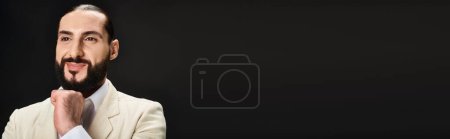 Photo for Joyful and bearded arabic man in white shirt and blazer looking at camera on black backdrop, banner - Royalty Free Image