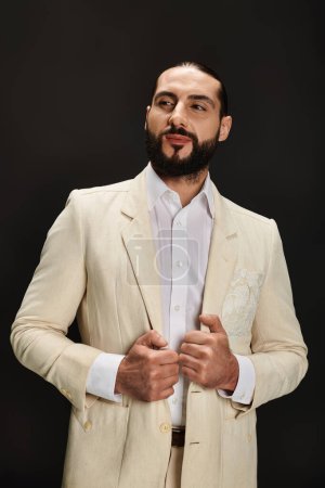stilvoller und bärtiger arabischer Mann in weißem Hemd und elegantem Blazer, der vor schwarzem Hintergrund wegschaut