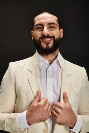 fröhlicher bärtiger arabischer Mann in weißem Hemd und Blazer, der in die Kamera auf schwarzem Hintergrund blickt