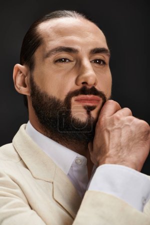 close up portrait of bearded and confident arabic man in elegant attire posing on black backdrop