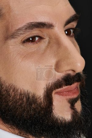 Nahaufnahme Porträt eines selbstbewussten arabischen Mannes mit braunen Augen, der vor schwarzem Hintergrund posiert und wegschaut