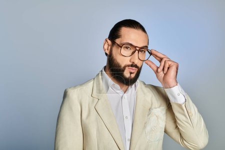 Foto de Hombre elegante y barbudo en gafas y atuendo blanco posando sobre fondo gris, ropa formal - Imagen libre de derechos