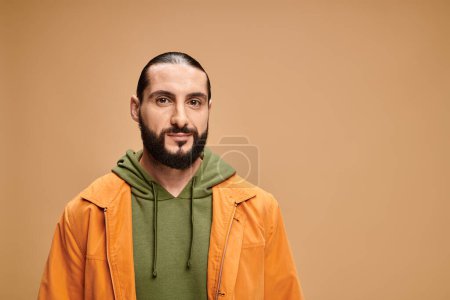 Porträt eines gutaussehenden und bärtigen arabischen Mannes in legerer Kleidung, der vor beigem Hintergrund in die Kamera blickt