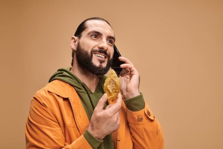 Foto de Hombre feliz sosteniendo postre tradicional de Oriente Medio y hablando en el teléfono inteligente en beige, baklava - Imagen libre de derechos