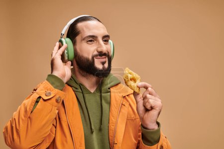 cheerful man in headphones holding honey baklava on beige background, middle eastern dessert