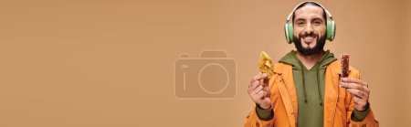 happy man in headphones holding two middle eastern desserts, honey baklava and churchkhela banner