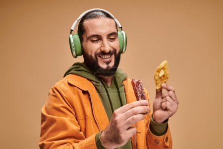 happy man in headphones holding two middle eastern desserts, honey baklava and churchkhela