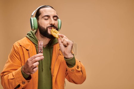 joyful man in headphones eating delicious honey baklava on beige backdrop, turkish delights