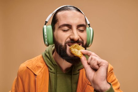 cheerful man in headphones eating delicious honey baklava on beige backdrop, turkish delights