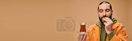 Banner eines glücklichen bärtigen Mannes, der türkischen Tee in einer traditionellen Glasschale hält und leckere Baklava isst