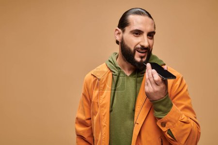 Foto de Feliz hombre de Oriente Medio con barba enviando mensaje de voz en fondo beige, teléfono inteligente - Imagen libre de derechos