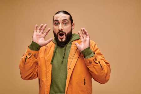 shocked middle eastern man with beard and open mouth gesturing on beige background, wow