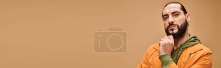Photo for Pensive middle eastern man touching beard and standing in casual attire on beige background, banner - Royalty Free Image