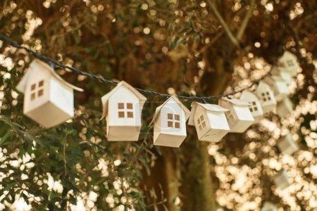 umweltfreundliche Girlande aus Holzhäusern auf grünem Baum mit frischem Laub im Gewächshaus
