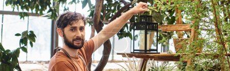 Téléchargez les photos : Heureux jardinier barbu en tablier de lin tenant lampe vintage près de rack dans la serre, bannière - en image libre de droit